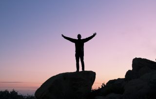 A man standing on top of a rock with his arms outstretched.