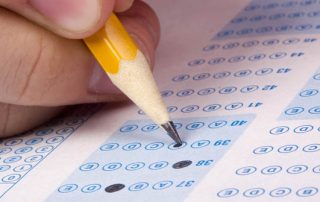 A person filling out an exam paper with a pencil.