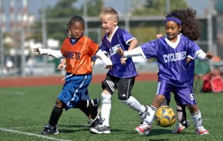 Three young children playing soccer on a field.